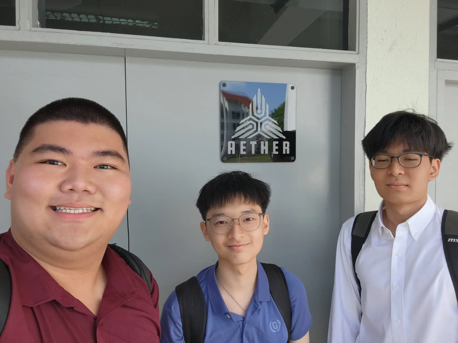 Three people taking a selfie outside a door bearing the AETHER name.