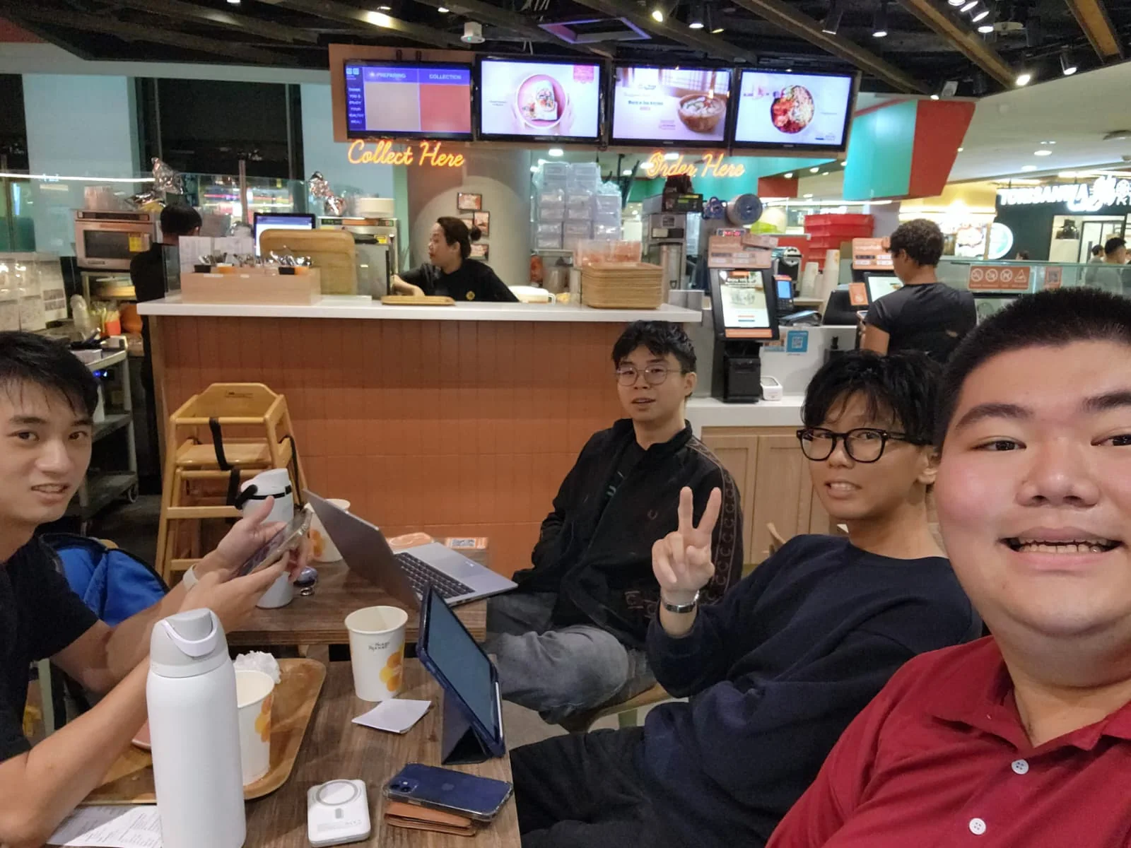 Four people gathered around a café table with laptops and drinks.